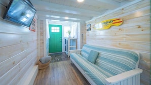 Interior acogedor de una cabaña con una puerta verde, un sofá a rayas, un televisor montado en la pared y un letrero que dice 'LANDSHARK'.