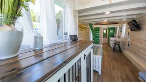 Interior de madera con cocina, una mesa de comedor y una escalera que sube a otro nivel.