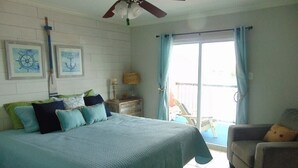 A bedroom with a bed, a chair, a ceiling fan, and a window with curtains. - A Wave From It  All! (Galveston)