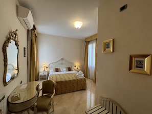 A hotel room with a bed, a chair, a table, and a mirror. - Angeles Inn (Venice)