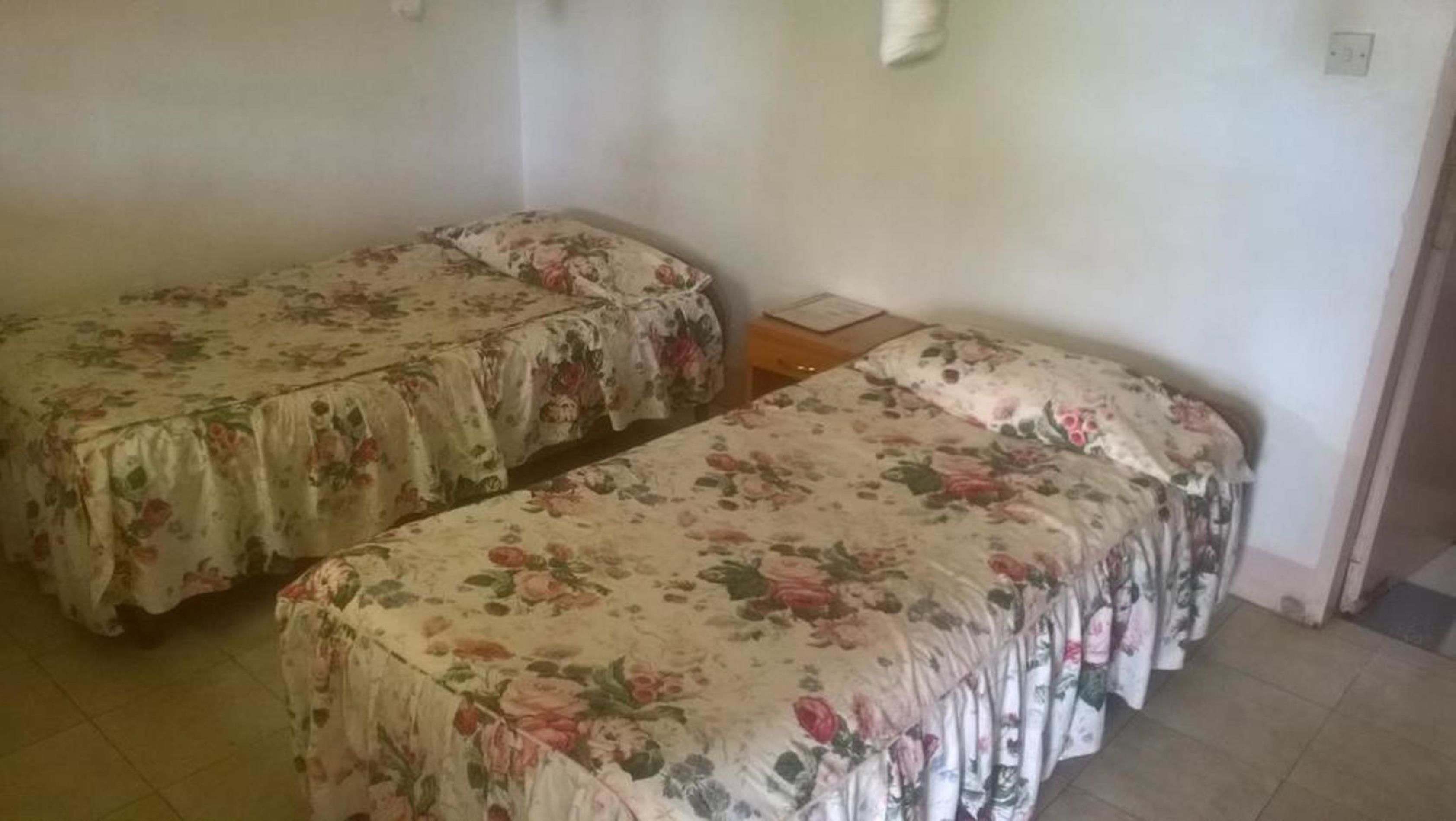 Una habitación con dos camas individuales, cada una con ropa de cama floral, una mesita de noche de madera y una lámpara de pared.