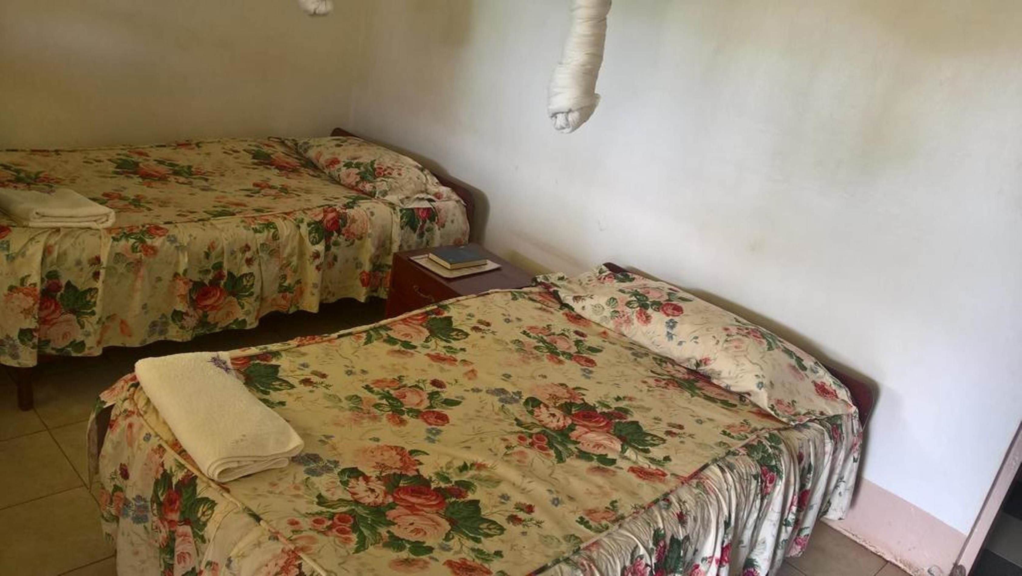 Two single beds with floral bedding in a room with plain walls and a tiled floor.