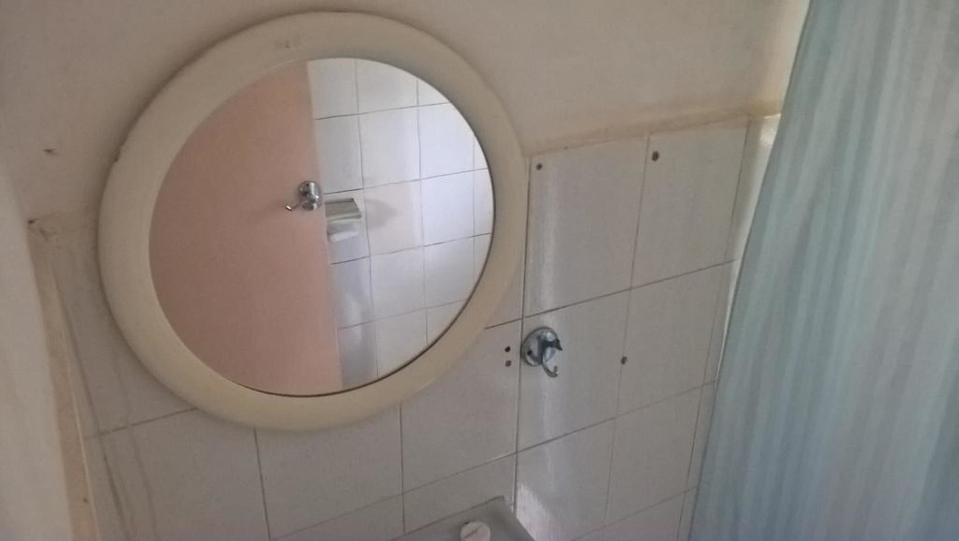 Un baño con espejo redondo, inodoro y zona de ducha.