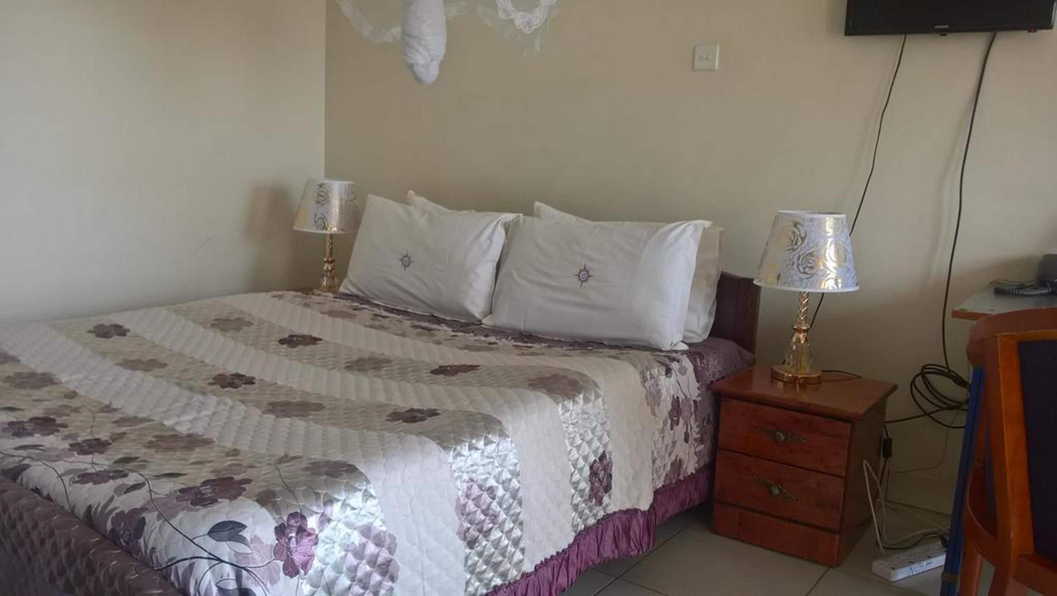 A bedroom with a bed, two bedside tables, a TV mounted on the wall, and a dresser.