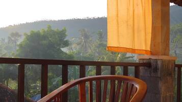 A wooden chair on a balcony with a view of a hilly landscape and palm trees.