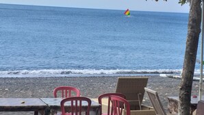 A beachside seating area with tables and chairs, overlooking the ocean. - Bali Sari Homestay (Karangasem)