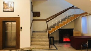 A modern interior with a marble staircase, a fireplace, and an elevator. - Hotel Chanakya (Agra)