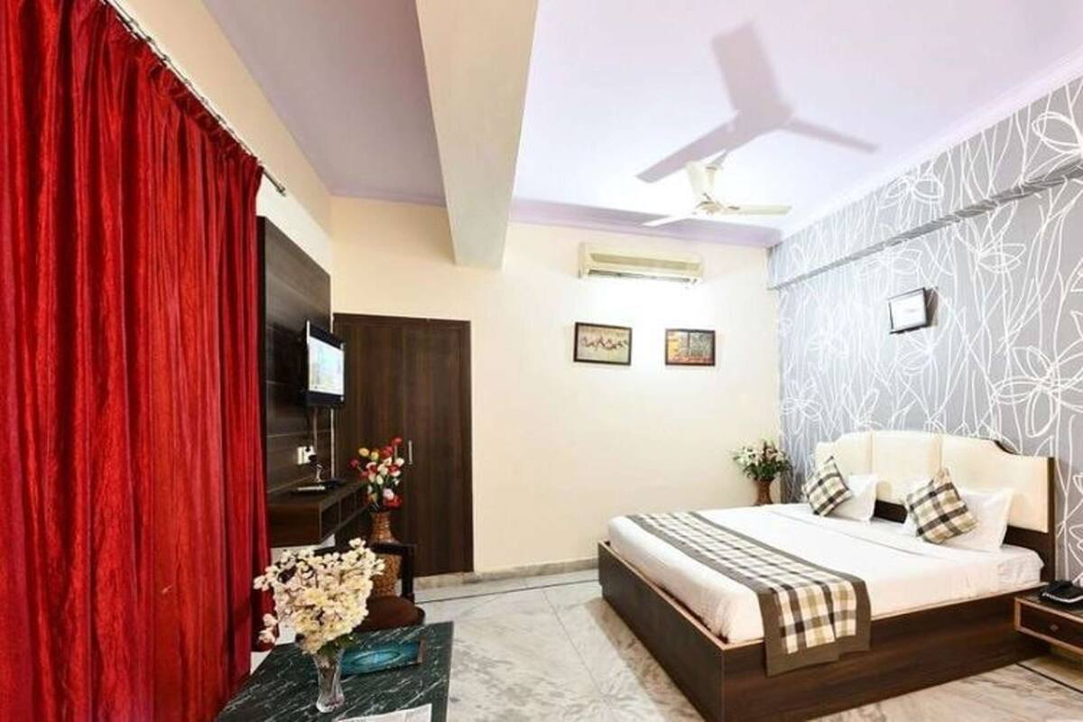 A hotel room with a bed, a desk, a TV, a ceiling fan, and a red curtain.