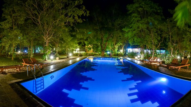 A nighttime swimming pool with clear water, surrounded by trees and outdoor seating areas. - Jays Holiday resort (Habarana)