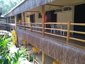 A building with a thatched roof, a balcony with a wooden railing, and a dining area with plastic chairs and tables. - Rc Sol de Boiçucanga Suites (São Sebastião)