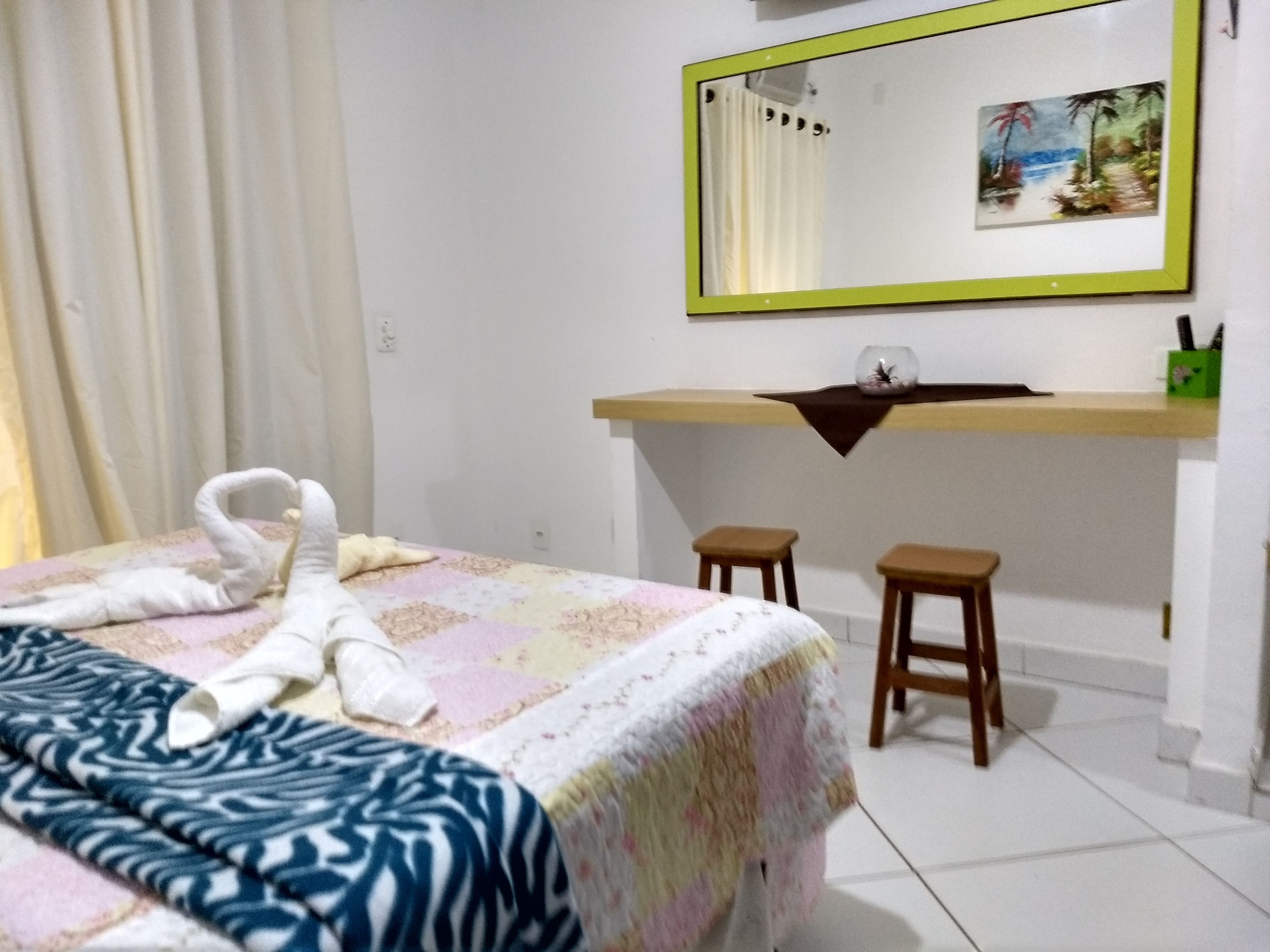 Ein Hotelzimmer mit einem Bett, einem Schreibtisch, zwei Hocker, einem Spiegel und einem Bild an der Wand.