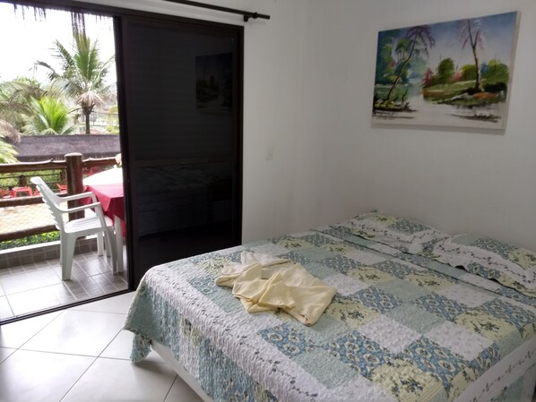 A bedroom with a bed, a painting on the wall, and a view of a balcony with chairs and a table.