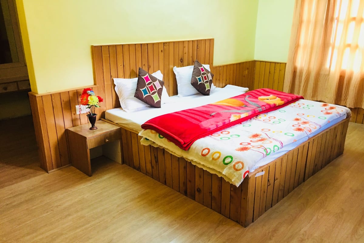 A wooden-framed bed with a floral-patterned bedspread and pillows, a nightstand with a vase of flowers, and a wooden floor.