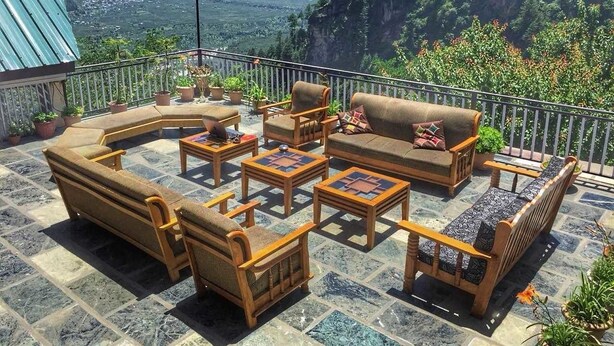 Een terras met buitenmeubilair, waaronder banken, stoelen en tafels, met een bergachtige achtergrond.
