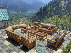 A terrace with outdoor furniture, including sofas, chairs, and tables, set against a mountainous backdrop. - Devdhar Hilltop Cottages (Manali)