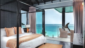 A modern bedroom with a large bed, a view of the ocean, and a balcony with wicker furniture.
