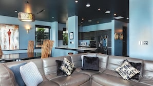 A modern living room with a leather sectional sofa, a dining table, and a kitchen in the background.