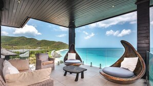 A covered outdoor seating area with wicker furniture and a view of the ocean.