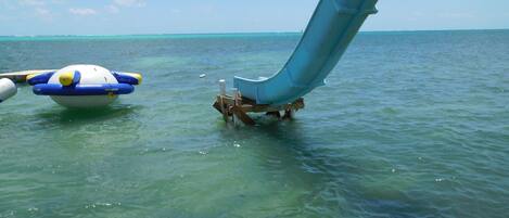 A clear blue sea with a water slide and a raft.