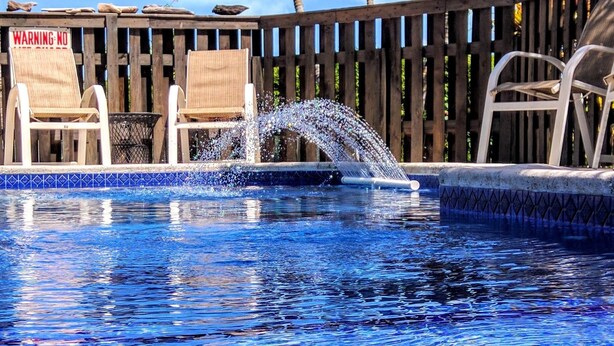 Una piscina amb una terrassa de fusta, palmeres i gandules.