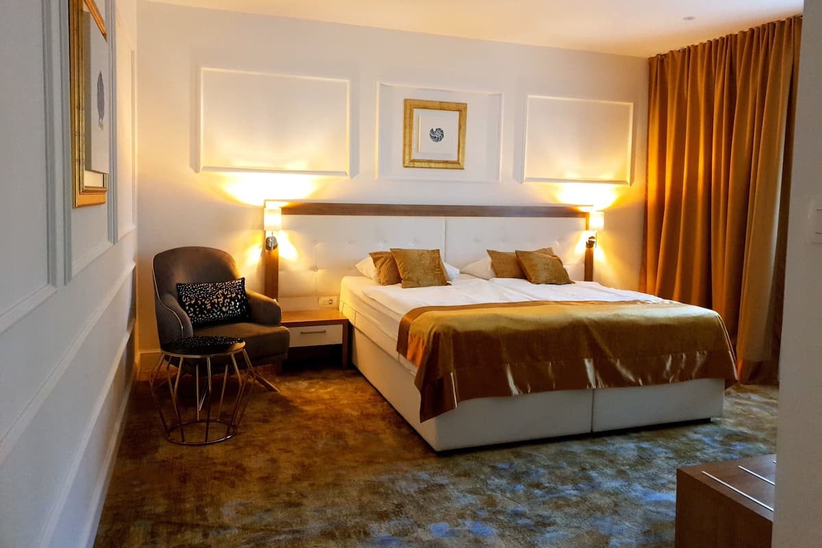 A hotel room with a large bed, two bedside lamps, a chair, and a small table.