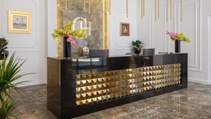 A reception desk with a black and gold design, flanked by two chairs and a vase of flowers. - Hotel Corner (Split)