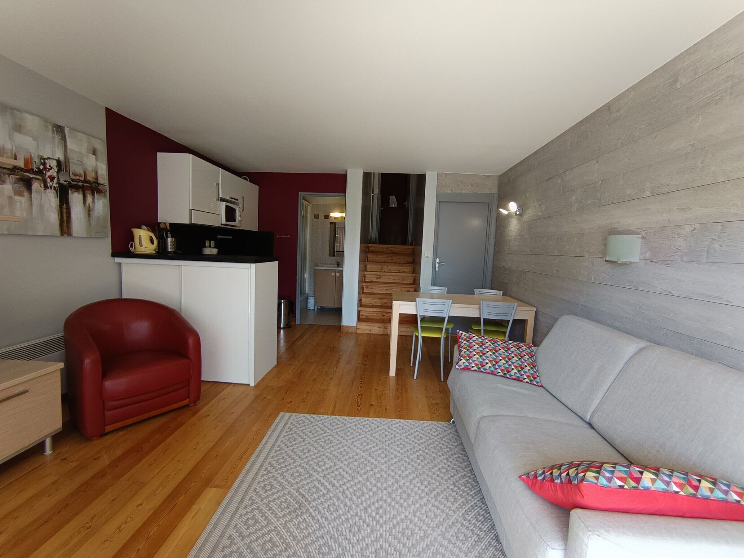 Un espace de vie compact comprenant un coin cuisine, un coin repas et un canapé agrémenté de coussins à motifs.