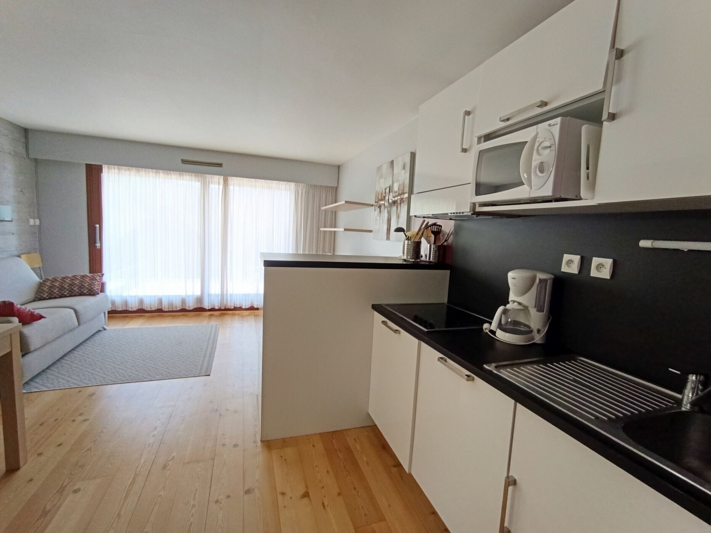 A modern kitchen with a black countertop, white cabinets, and a built-in microwave. There is a coffee maker on the counter and a window with curtains in the background.