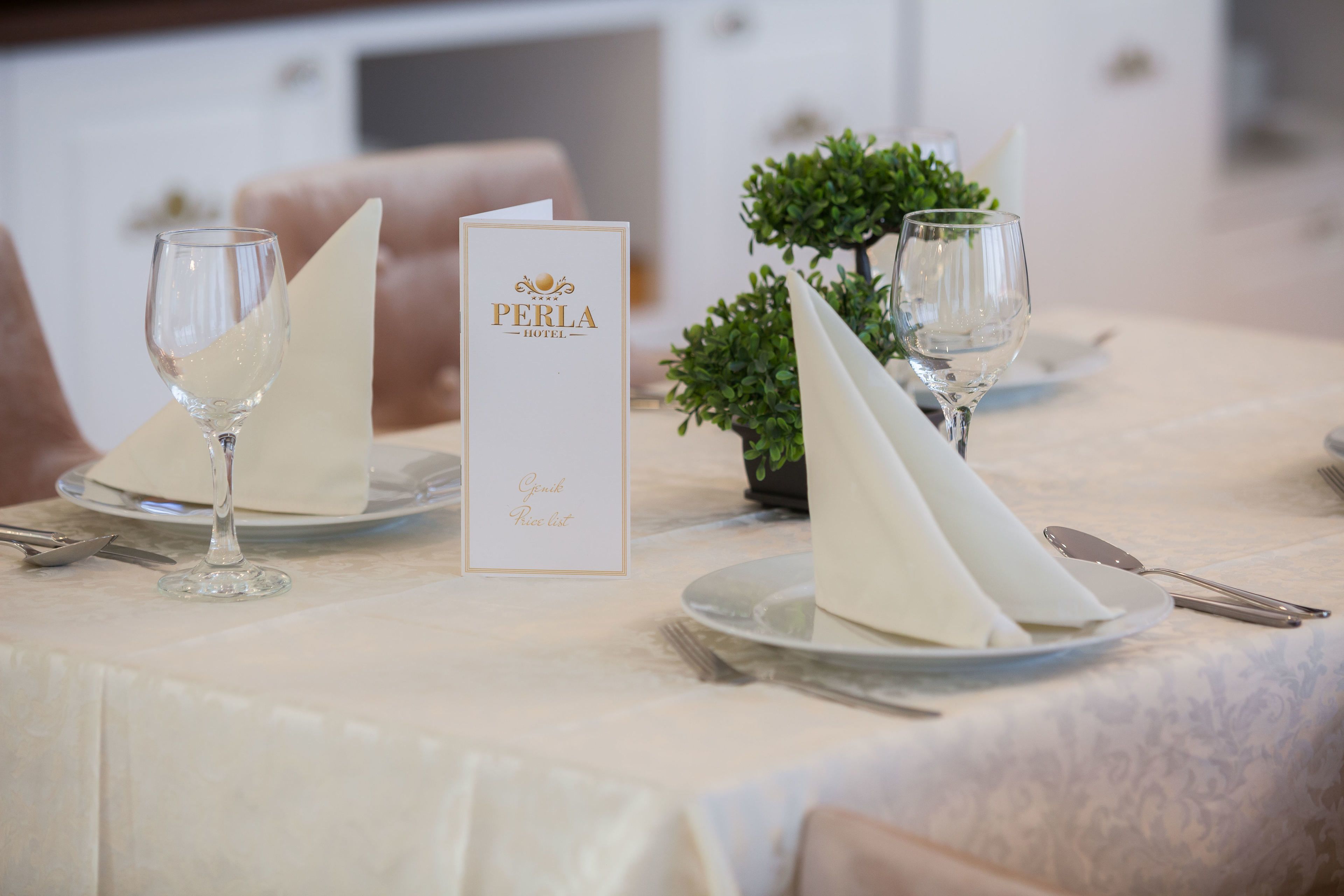 A table set with white napkins, wine glasses, and a menu for a hotel named PERLA.