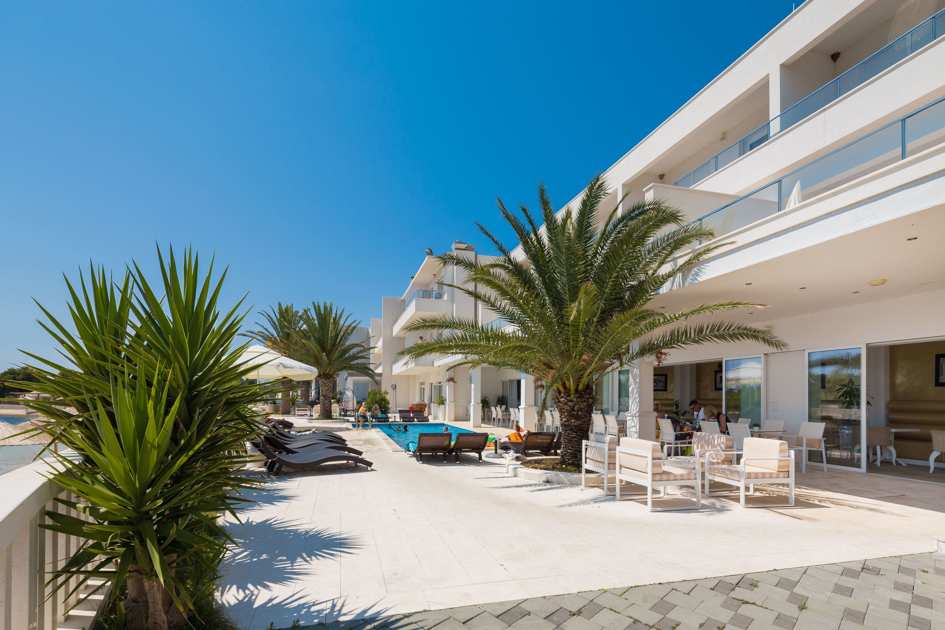 A poolside area with lounge chairs, palm trees, and a clear blue sky.