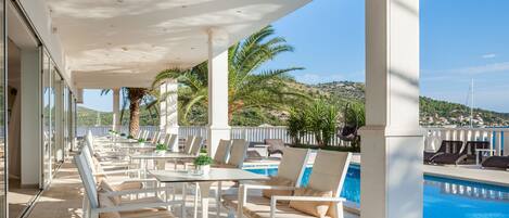 A covered outdoor area with a pool, lounge chairs, and a view of the landscape.