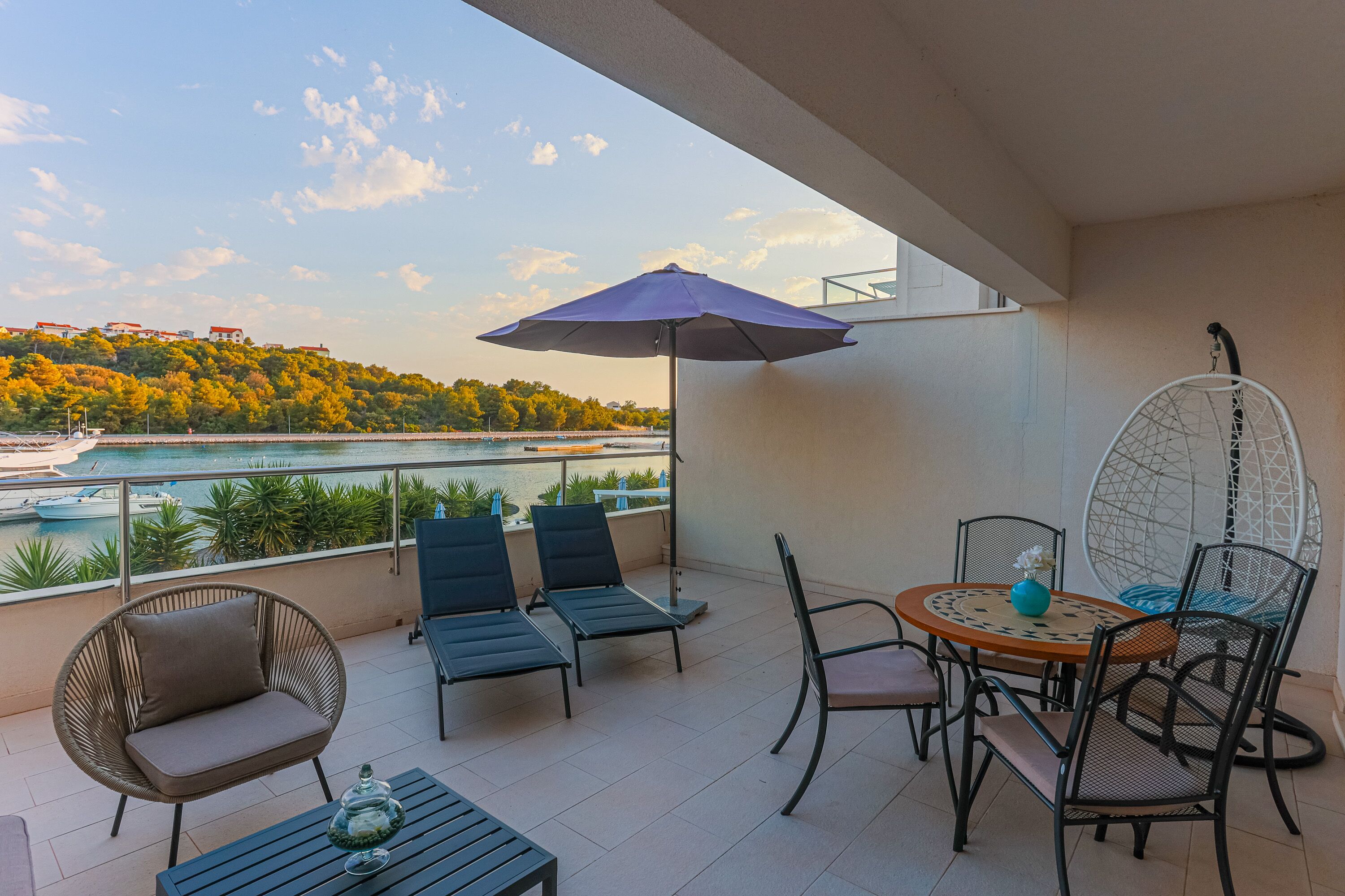 Un balcon donnant sur une étendue d’eau, une table avec des chaises et un fauteuil suspendu.