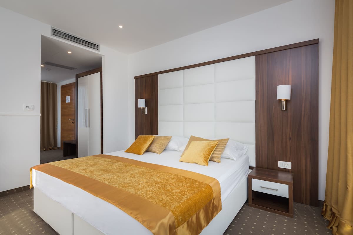 A hotel room with a large bed, a wooden headboard, a bedside table, and a wall-mounted lamp.