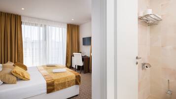 Een hotelkamer met een bed, een bureau, een stoel, een televisie en een douche.