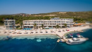Un hotel con varios pisos, piscina y zona de playa con sombrillas y sillas reclinables.