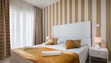 A neatly made bed with a white headboard, a bedside table with a lamp, and striped wallpaper.