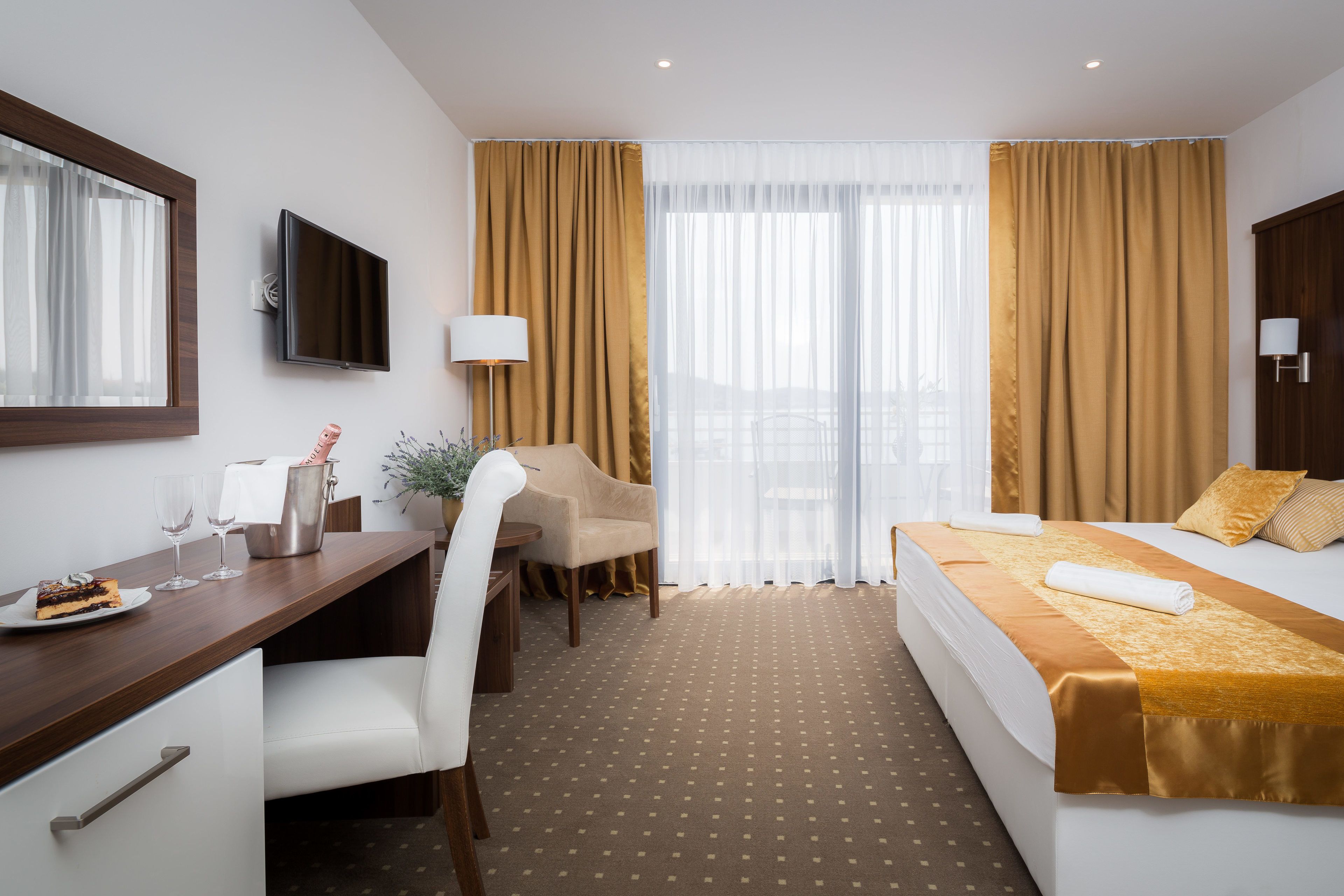 Habitación de hotel con cama, escritorio, silla, televisión y ventana con cortinas.
