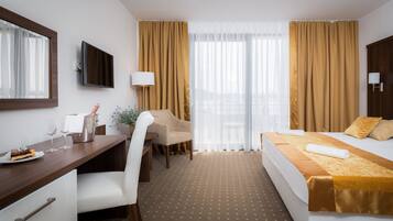 Habitación de hotel con cama, escritorio, silla, televisión y ventana con cortinas.