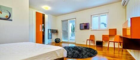 A modern bedroom with a bed, a black furry rug, wooden flooring, a TV, and a desk with chairs.