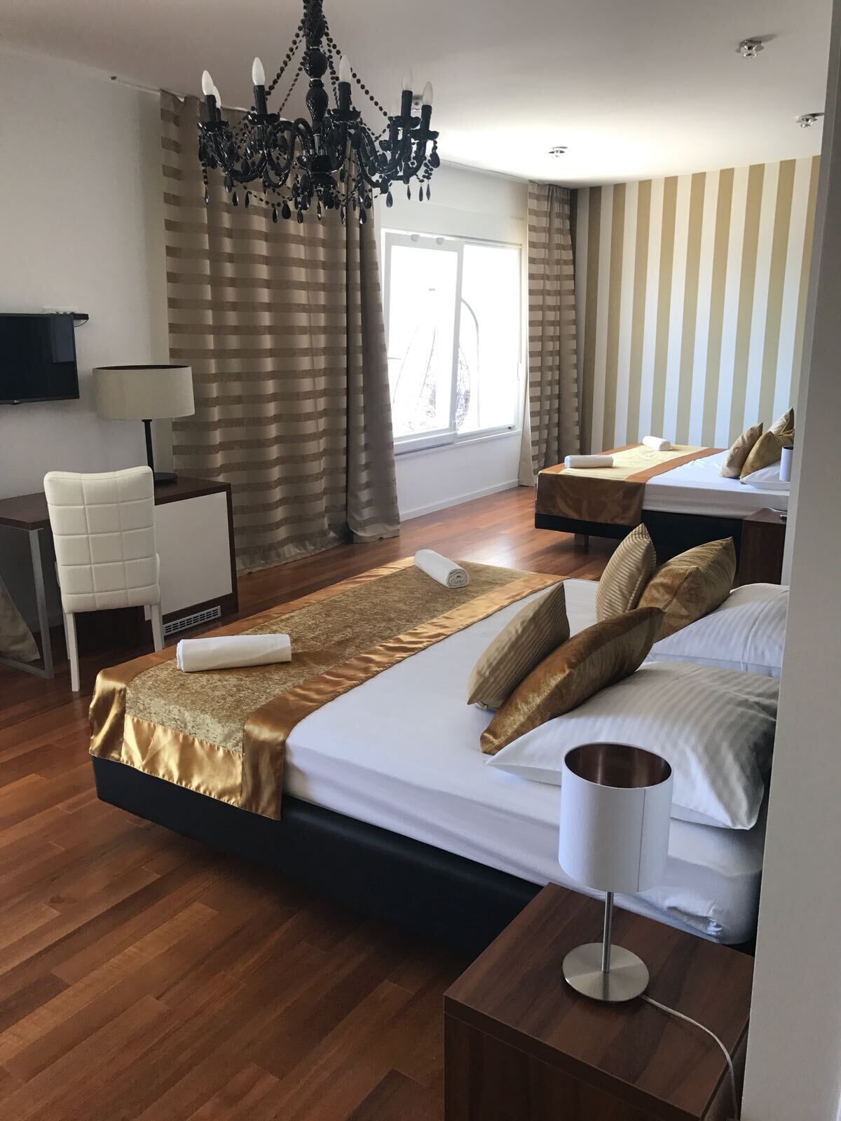 A hotel room with a large bed, a desk, a chair, a TV, and a chandelier.