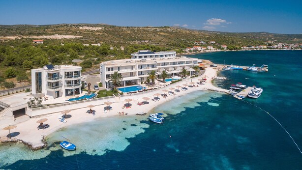 Un hotel frente al mar con varios balcones, una zona de piscina y barcos amarrados en el muelle.