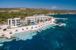 Un hotel frente al mar con varios balcones, una zona de piscina y barcos amarrados en el muelle.