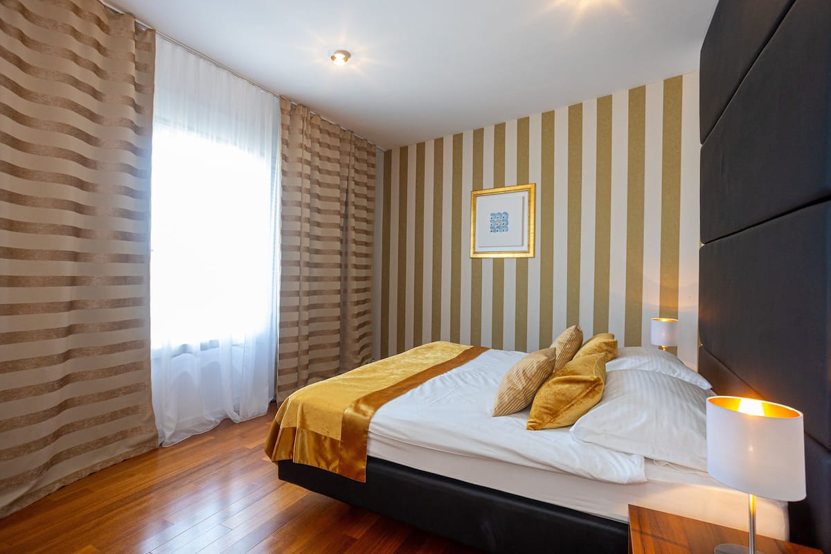 A hotel room with a bed, curtains, a wall with vertical stripes, and a framed picture.
