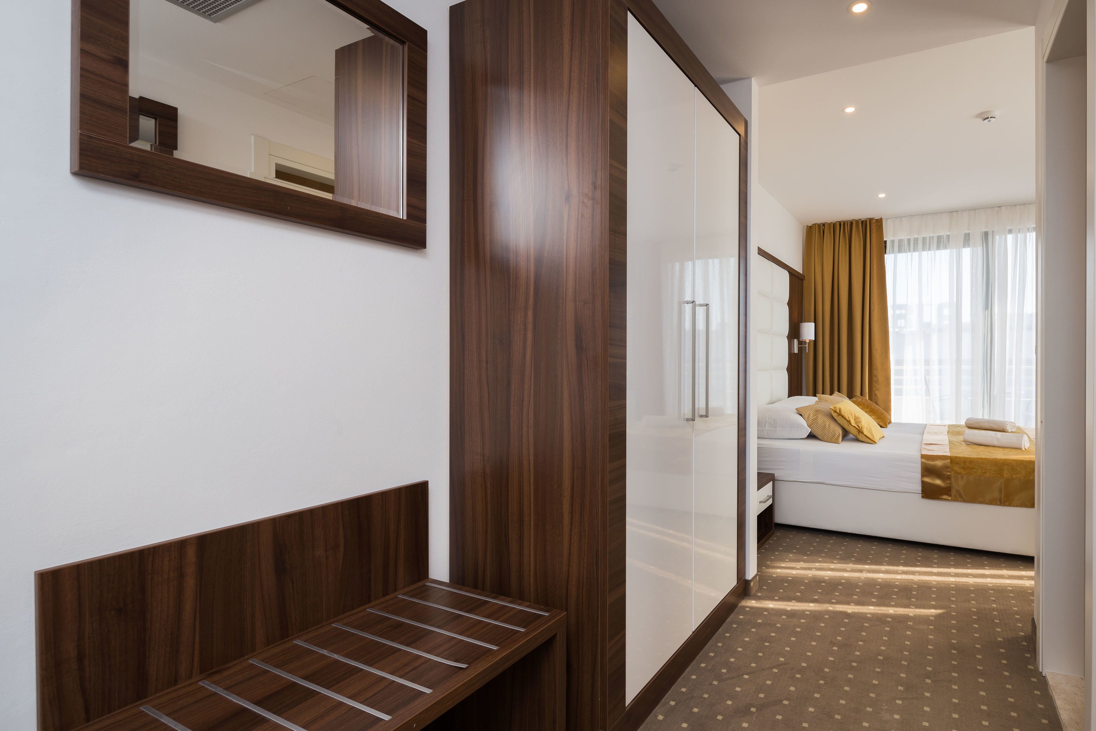 Ein Hotelzimmer mit einer hölzernen Bank, einem Bett mit brauner Bettdecke und einem großen Spiegel an der Wand.