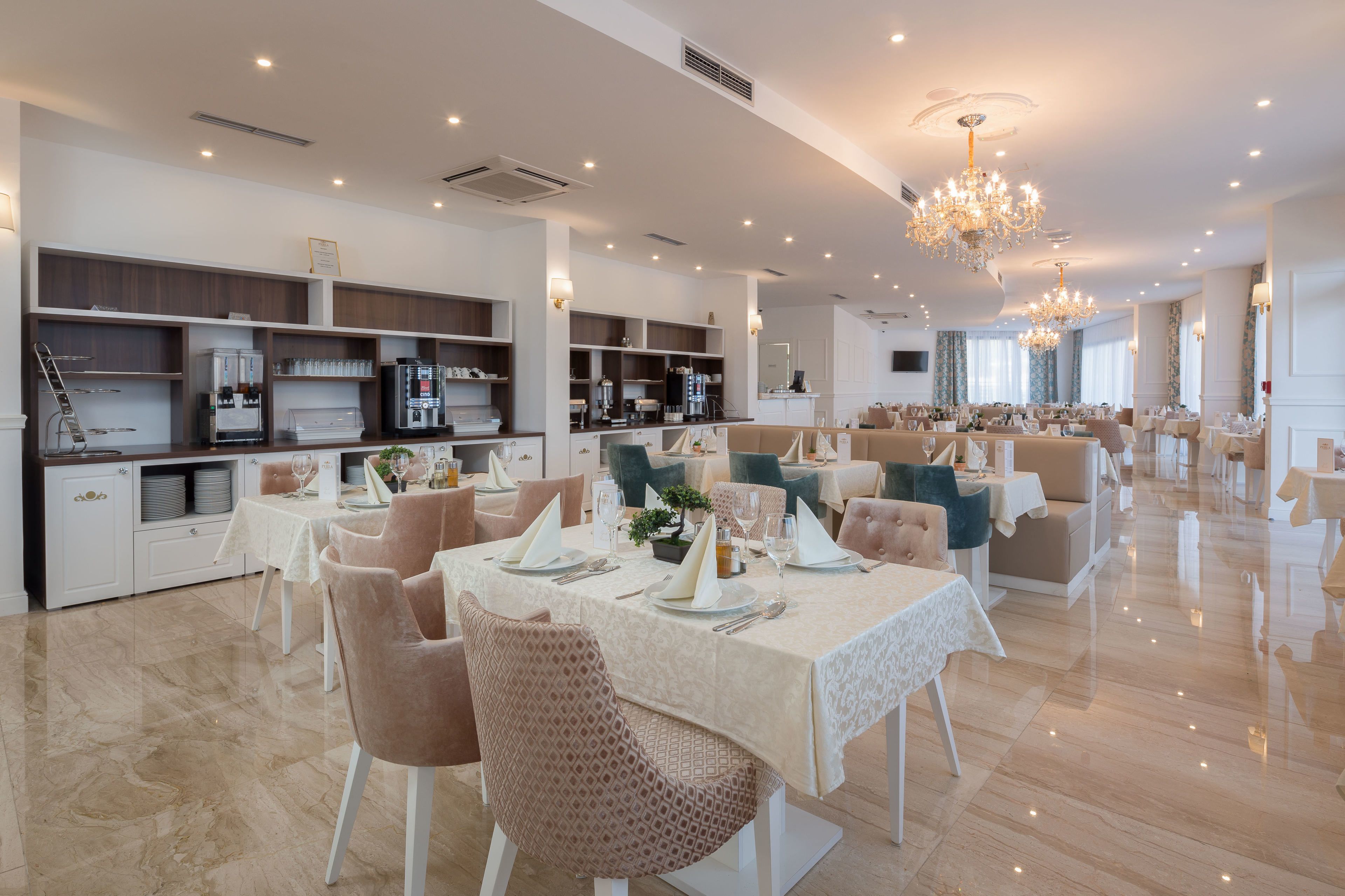 A spacious dining area with multiple tables set for service, a kitchen area with modern appliances, and a chandelier for lighting.