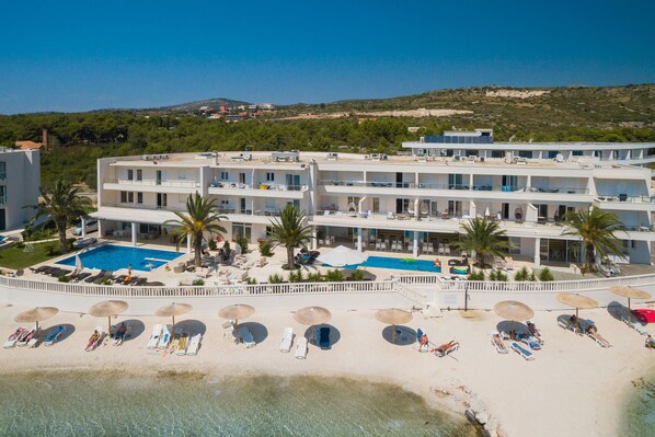 Un resort con piscina, playa con tumbonas y sombrillas, y vista al mar.