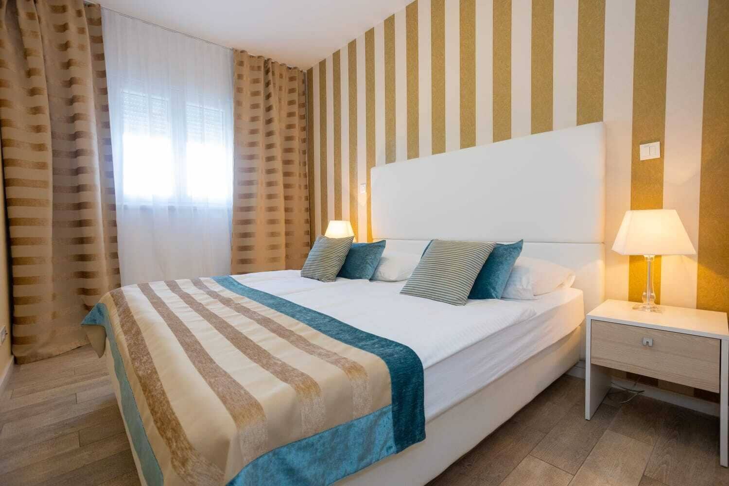 A hotel room with a large bed, striped curtains, a bedside lamp, and a nightstand.