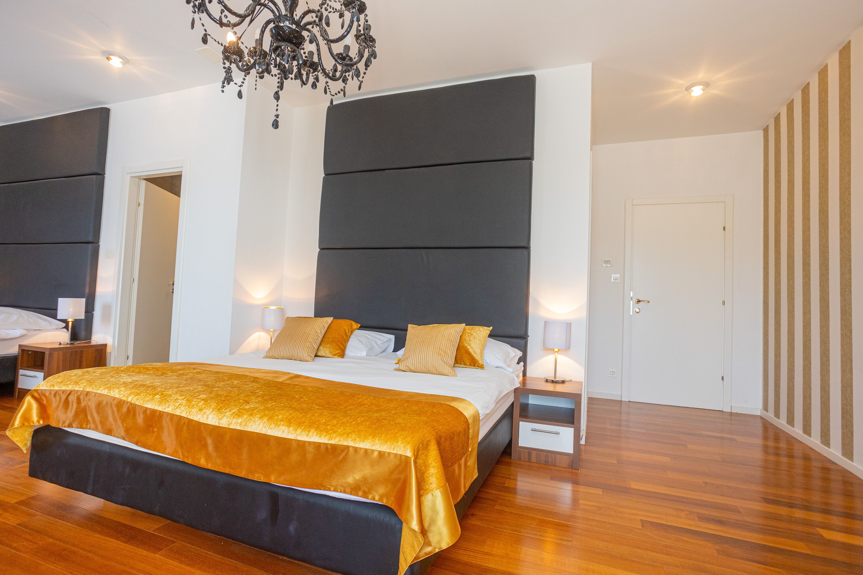 A modern bedroom with a large bed, bedside tables, a chandelier, and a door.