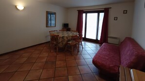 A room with a tiled floor, a dining table with chairs, a sofa, a TV, and a window with curtains. - Apartment centrally located near slopes, pets allowed, parking included (Montgenèvre)