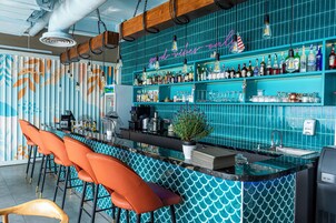 A bar area with a teal tiled backsplash, orange bar stools, and a variety of bottles and glasses on shelves.